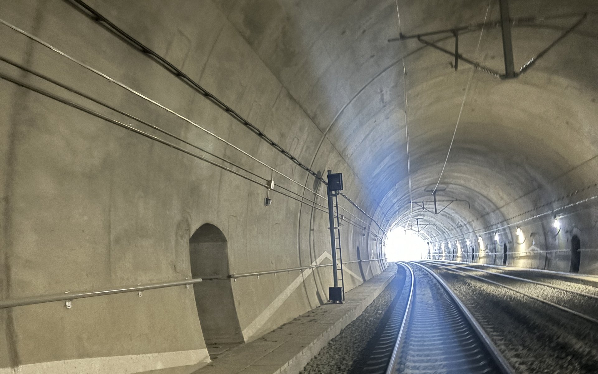 Cablu radiant instalat de-a lungul peretelui unui tunel feroviar, cu portalul în fundal