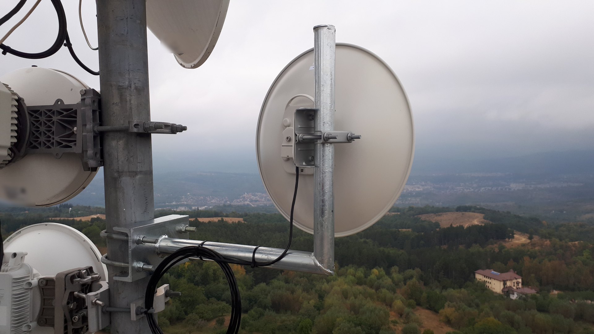 Antenă de radioreleu Cambium instalată pe pilon, cu o vale împădurită în fundal