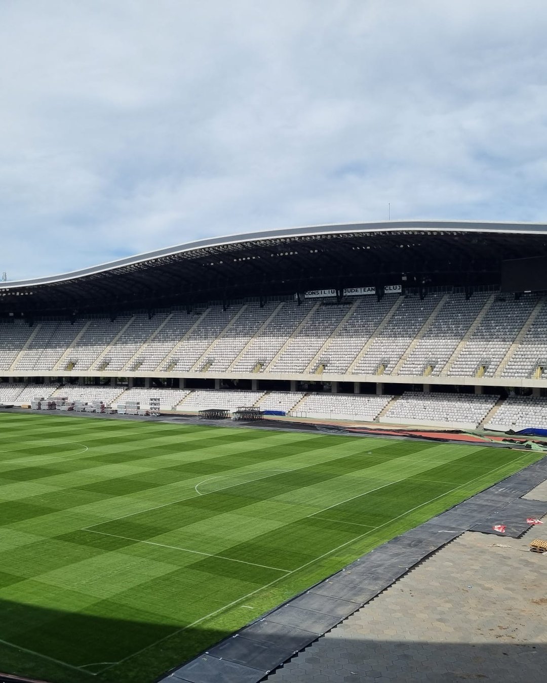 Tribuna principală a Cluj Arena văzută de la nivelul gazonului, cu acoperișul curbat deasupra scaunelor albe