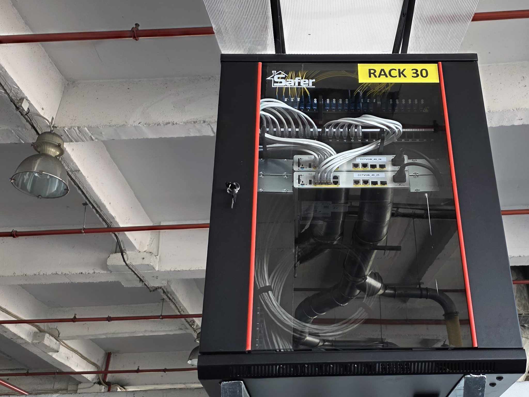 Rack suspendat cu patch panel de fibră optică și switch-uri etichetate, într-o hală industrială