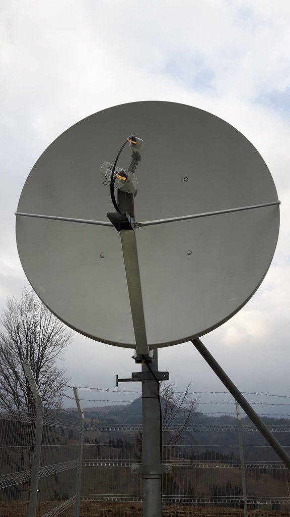 Antenă VSAT pe un site montan împrejmuit, cu munții în fundal
