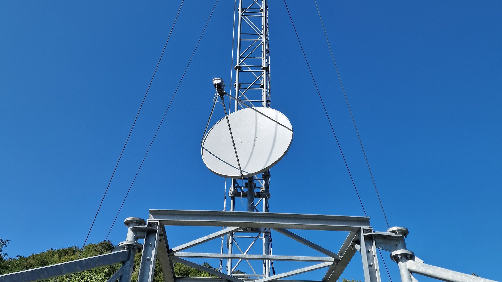 Antenă VSAT montată pe un pilon zăbrelit ancorat, pe cer senin, la un site izolat