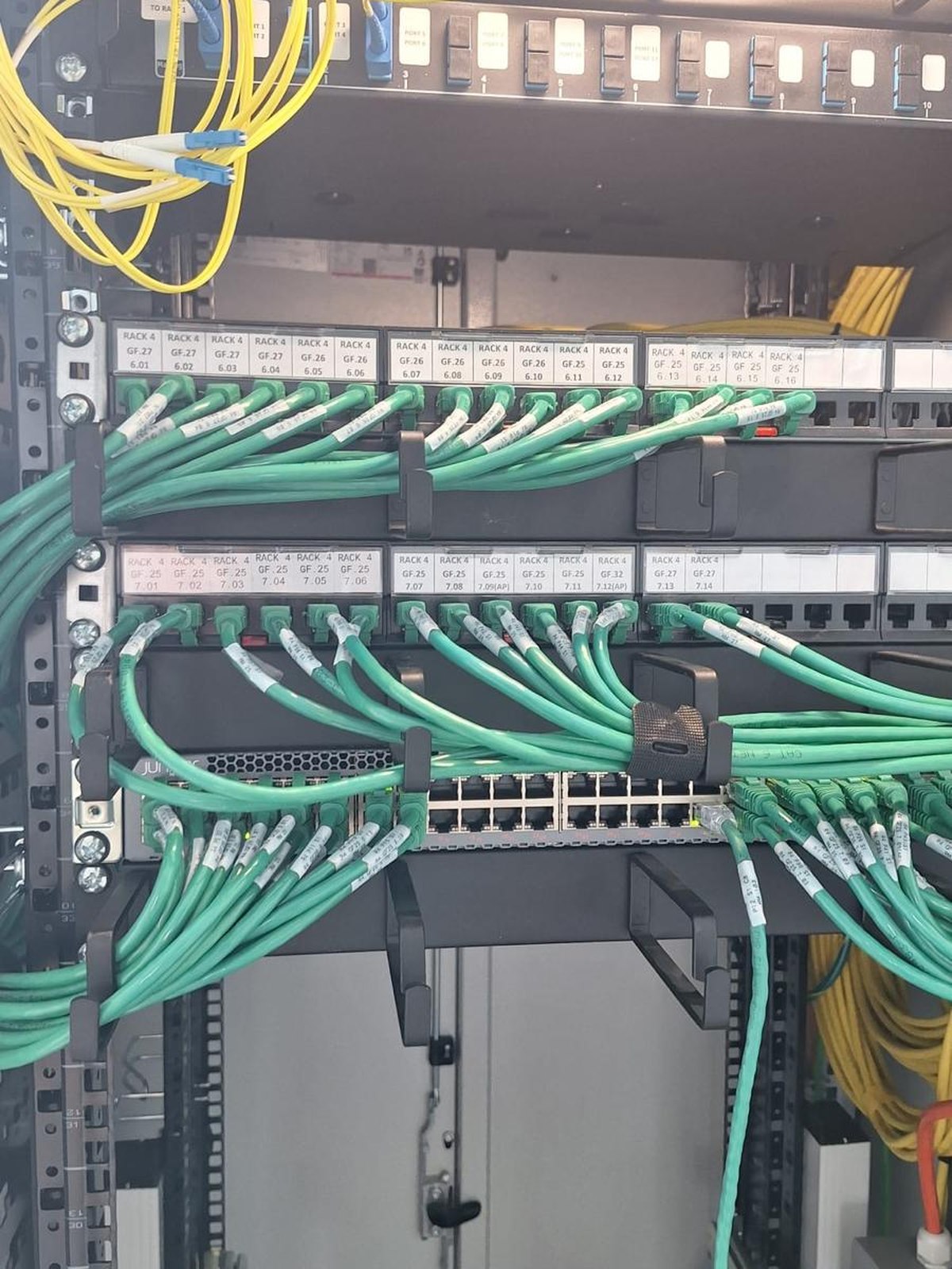 Green patch cords connected to the rack equipment, with the yellow fiber arriving in the panel above
