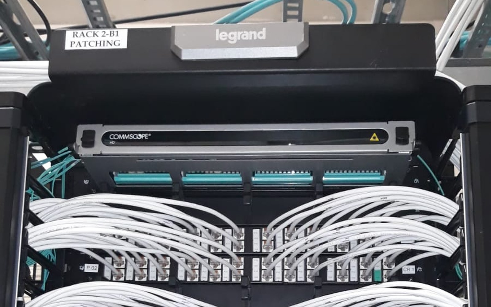 Câmp de patch CommScope cu patchcord-uri albe organizate, în rack-ul de distribuție Legrand